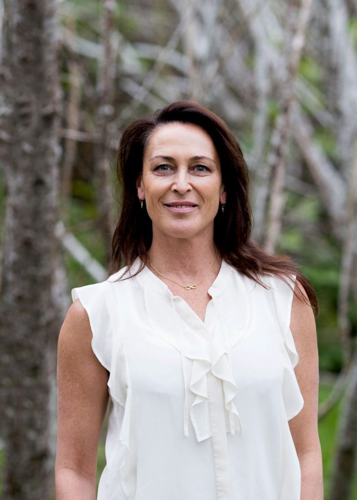 Portrait shot of Susan wearing a white blouse, smiling in nature