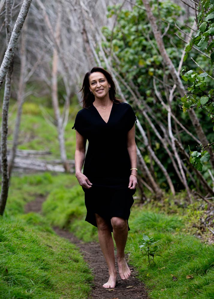 Susan walking along a bush path, smiling and wearing a black dress